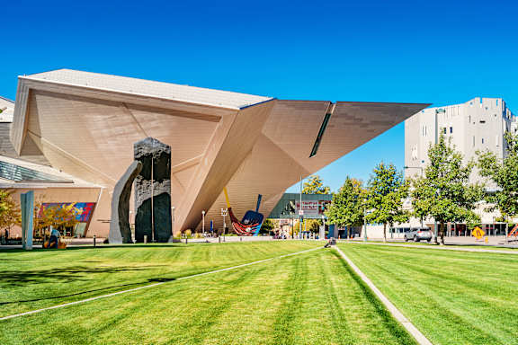 A large building with a unique design sits in the middle of a grassy field.