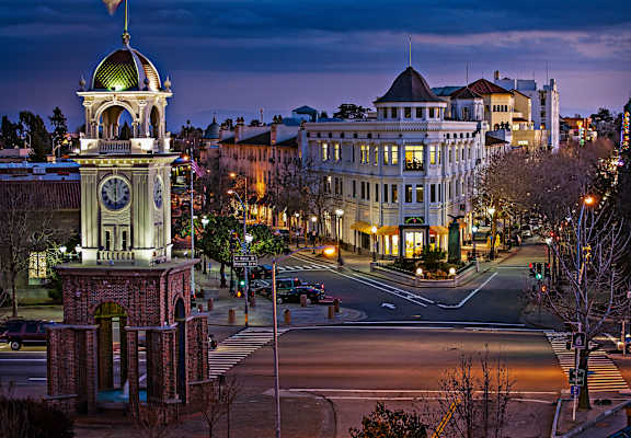 A clock tower stands in front of a building with a street in front of it.