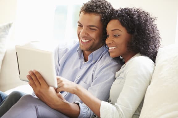 a couple sitting on a couch looking at a tablet at Sandy Creek Apartments, Texas