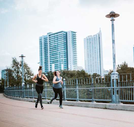two women running on a bridge with the city in the background