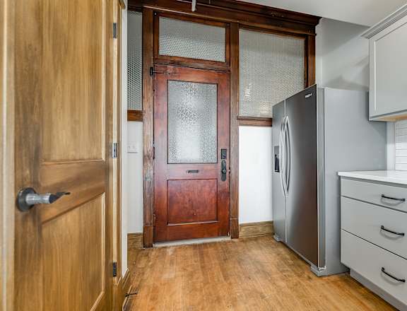 A kitchen with a wooden door and a stainless steel refrigerator.