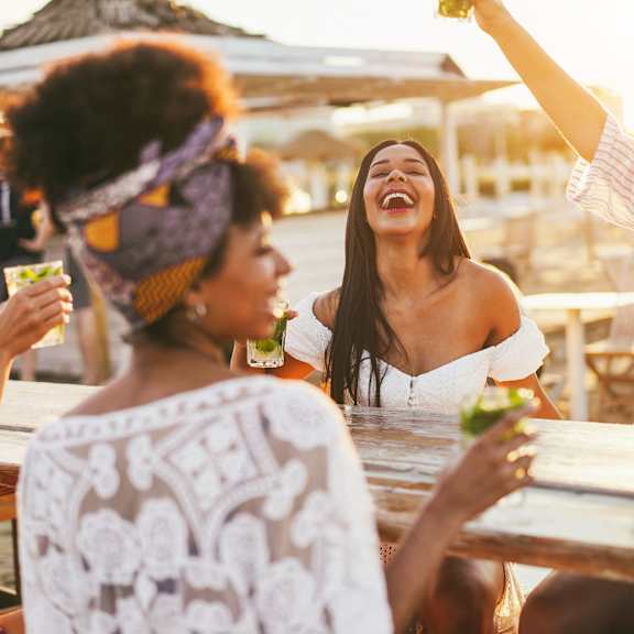 a group of women sitting at a table laughing and drinking