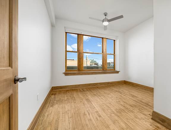 A room with a ceiling fan and a window overlooking a cityscape.