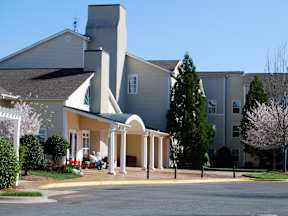A church with a green roof and a white steeple is surrounded by a parking lot.