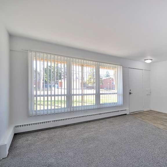 A room with a carpeted floor and a window with blinds.