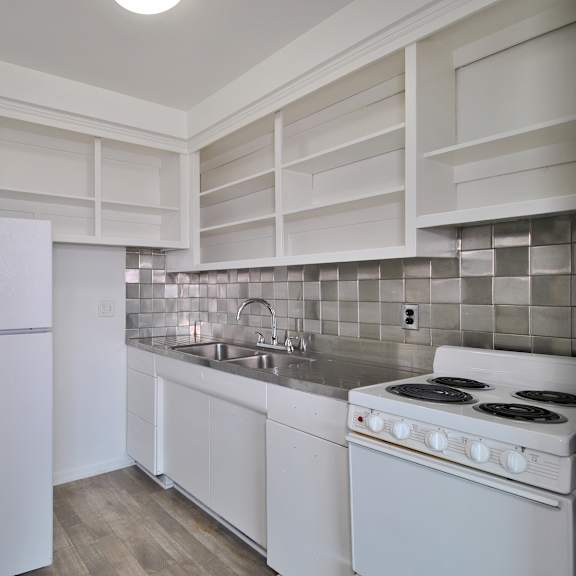A white kitchen with a refrigerator, sink, and stove.