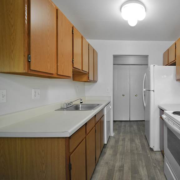 Galley kitchen with wood cabinets and white appliances at Garfield Commons in Clinton Township, MI