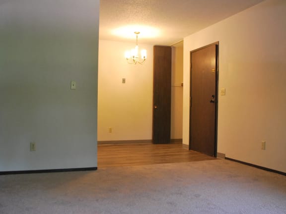 an empty living room with a hard wood floor and a door to a bedroom