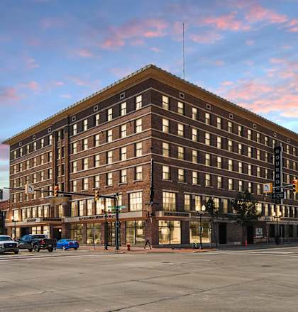 A large brown building with many windows is in the foreground with cars parked in front.