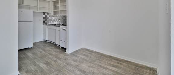 A kitchen with white cabinets and a refrigerator is visible from the living room.