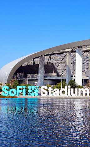 A large stadium with a semi-circular roof and a body of water in the foreground.