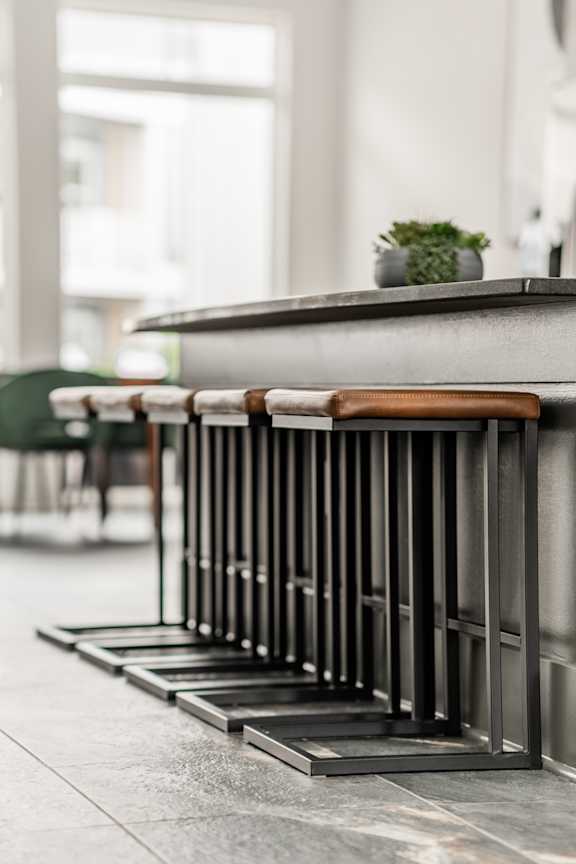 A row of black metal stools with wooden seats are lined up in front of a grey counter.