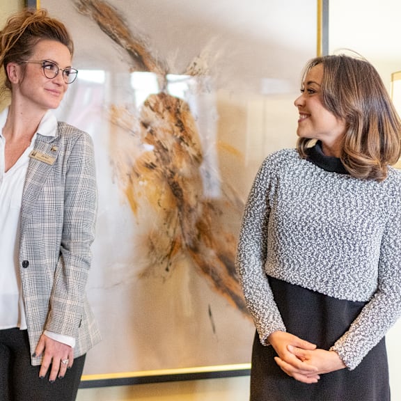 Two women standing in front of a piece of art in the lobby at Windscape Apartment Homes. 