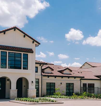 A large white building with a red tile roof and a black fence in front. at Northwoods, Texas