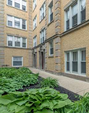 Exterior courtyard at Berteau Manor apartments in Chicago’s Lakeview neighborhood featuring landscaped greenery and classic brick architecture.
