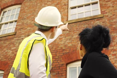 a man wearing a hard hat and pointing at a brick building