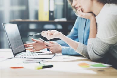 two women sitting at a desk using a laptop computer