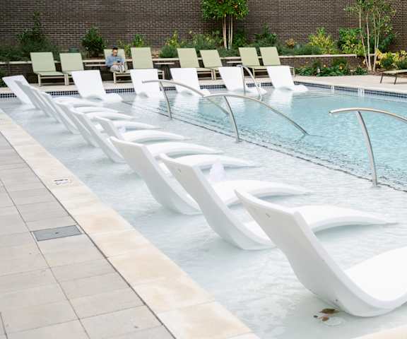 A row of white lounge chairs are lined up along the edge of a pool at Anthem House, Huntsville, Alabama