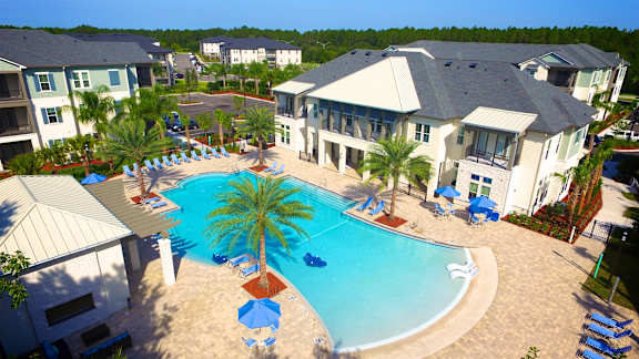 a large swimming pool with palm trees in front of a large apartment complex at Alaqua, Florida, 32258 at Alaqua Apartments, Florida, 32258