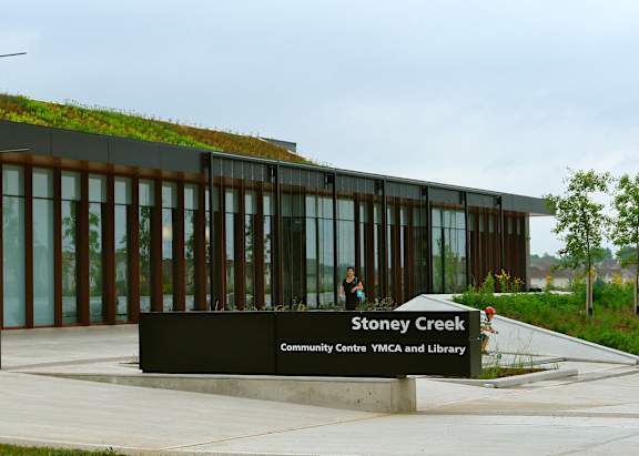 A modern building with a green wall on the side and a sign that says Stoney Creek Community Centre YMCA and Library.