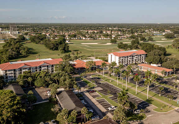 A large building with a red roof is surrounded by a parking lot.