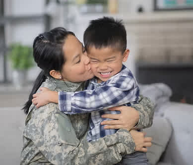 A woman in military uniform hugs a young boy.