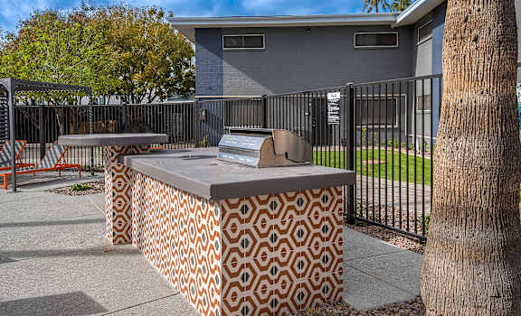A concrete bench with a patterned back rest sits in front of a black fence.