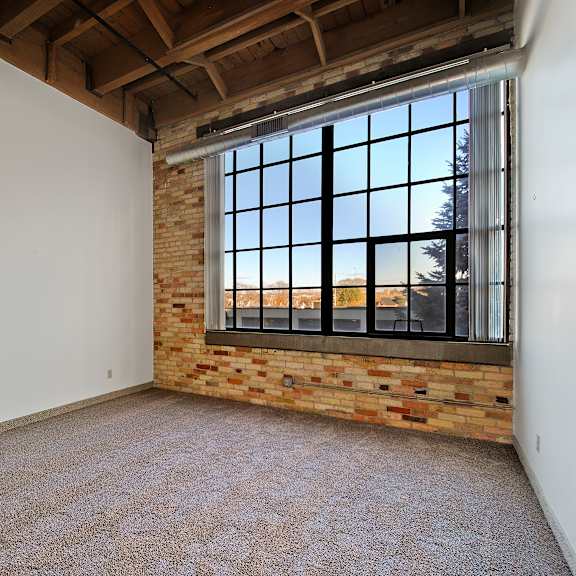 Loft room with a large factory-style window and exposed brick at Off Broadway Apartments