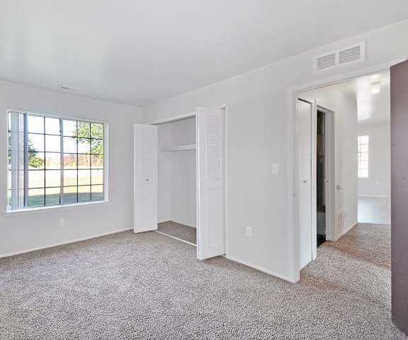 A large empty room with a window and carpeted floor.