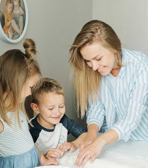 A woman and two children are making cookies together.