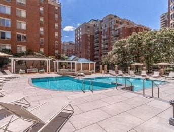 A large swimming pool surrounded by sun loungers and umbrellas in a courtyard.