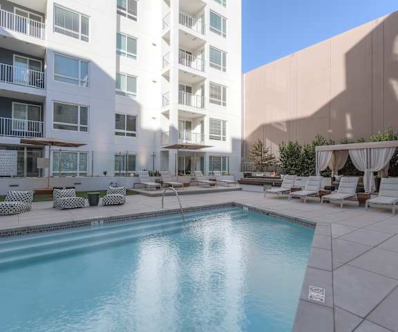 A swimming pool in a courtyard surrounded by chairs and umbrellas.