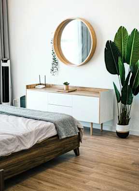 A bedroom with a bed, a mirror, and a plant.