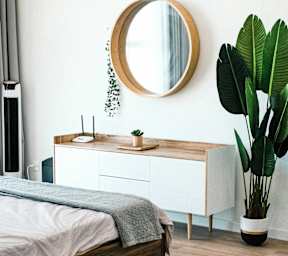 A round mirror hangs on a white wall above a wooden bed.