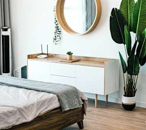 A round mirror hangs on a white wall above a wooden bed.
