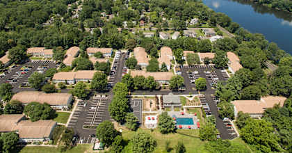 A bird's eye view of a parking lot surrounded by trees and buildings with a river in the background.
