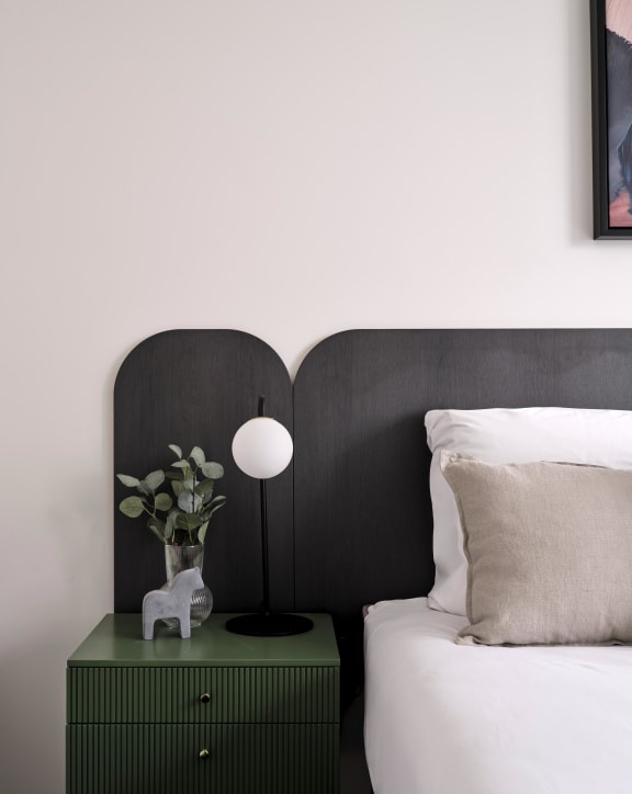 a bedroom with a bed and a green nightstand with a lamp and a plant