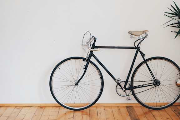 A black bicycle with a white seat and handlebars is leaning against a white wall.