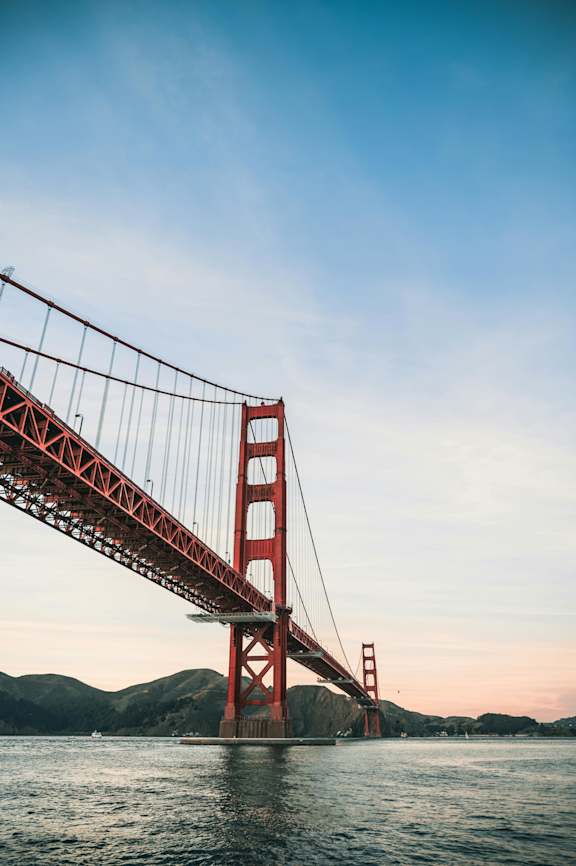 A red suspension bridge spans across a body of water.