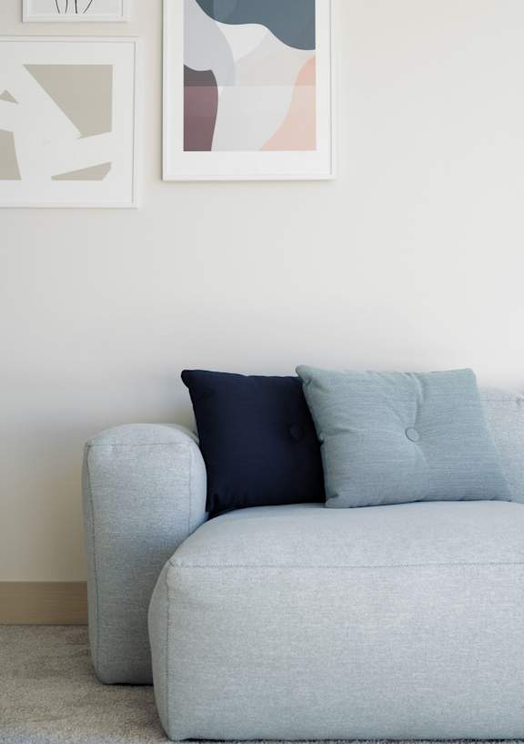 A grey couch with two pillows sits in front of a wall with artwork.