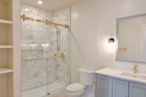 A white bathroom with a marble shower and a toilet.