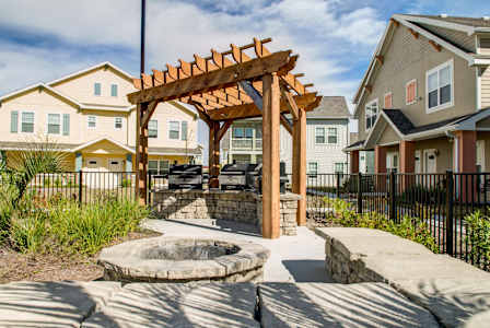 A wooden pergola is in the middle of a courtyard with a fire pit.