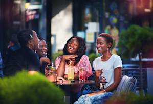 Four people are sitting at a table outside, laughing and enjoying drinks.