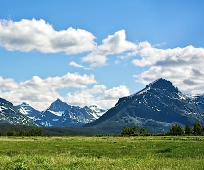 A mountain range with snow-capped peaks under a blue sky with scattered clouds.