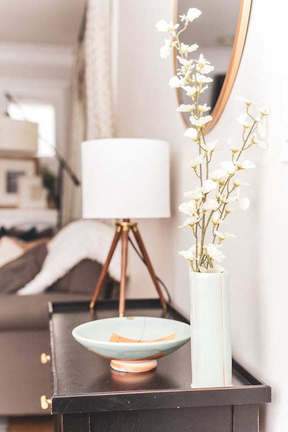 A white vase with white flowers sits on a black table next to a white lamp at Coast Pine