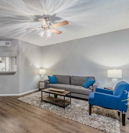 A living room with a grey couch, a blue chair, and a dining table.