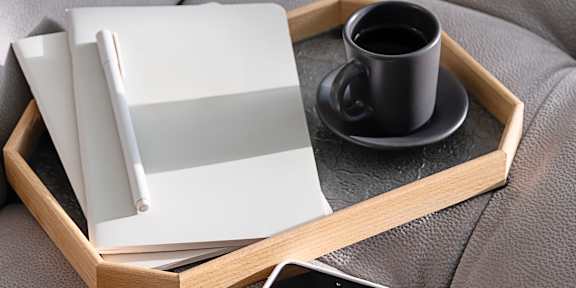 A tray with a cup of coffee, a book, and a smartphone on a grey couch.