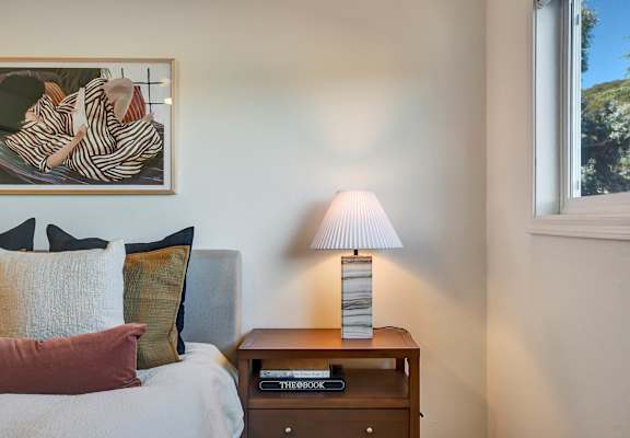 A bedroom with a bed, a nightstand with a lamp and a painting on the wall.