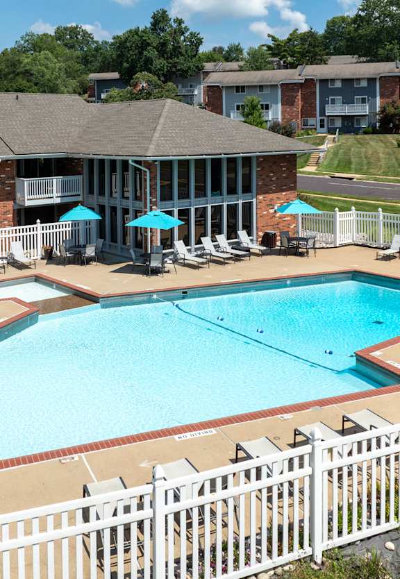 A white fence surrounds a small pool with a white building in the background.