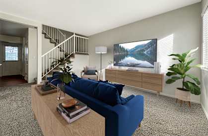 A living room with a blue couch, a wooden coffee table, a staircase, and a large painting on the wall.